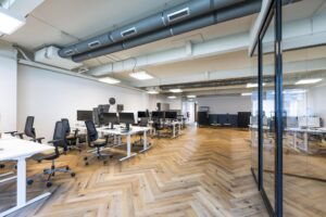 Moderne kantoorruimte aan de De Ruijterkade met open werkplekken, houten visgraatvloer en glazen scheidingswand.
